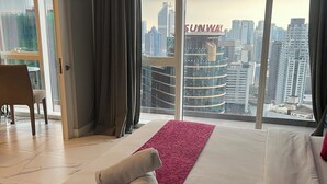 A hotel room with a large bed, a red decorative runner, a rolled towel, and a view of a cityscape with tall buildings. - Platinum Suites Kuala Lumpur by Skyline (Kuala Lumpur)