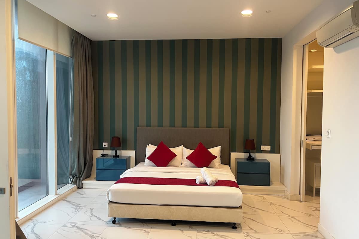Una habitación de hotel moderna con una cama grande, dos mesitas de noche, un ventanal con cortinas, una pared a rayas y suelo de mármol.