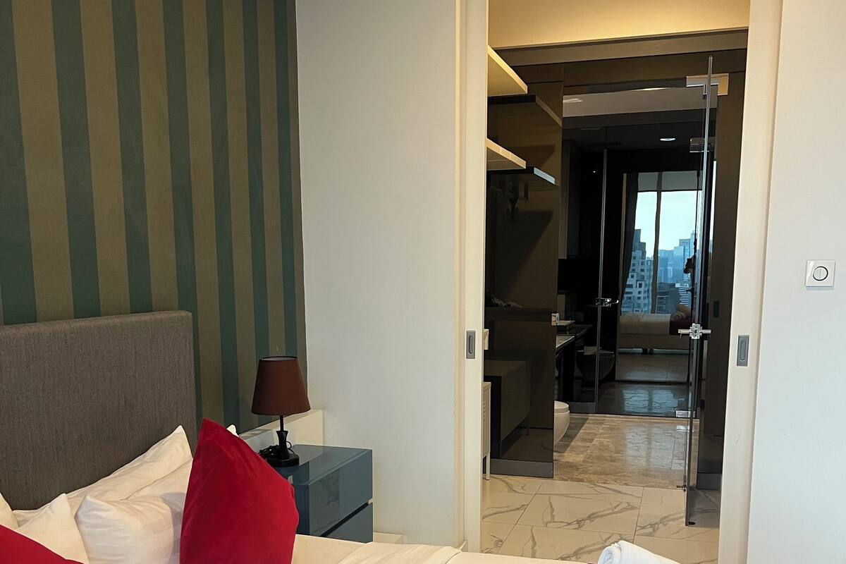 Habitación de hotel con cama, mesita de noche, almohada roja, almohada blanca, manta roja y una toalla sobre la cama.