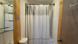 Ein kleines Badezimmer mit einem Holzbadezimmerhocker, einem weißen Waschbecken, einer Toilette und einer Duschvorhang.