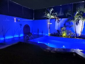A swimming pool with a blue-lit deck, surrounded by palm trees and tropical plants. - HOUSE WITH SWIMMING POOL IN CUAUTLA DOWNTOWN (Cuautla)
