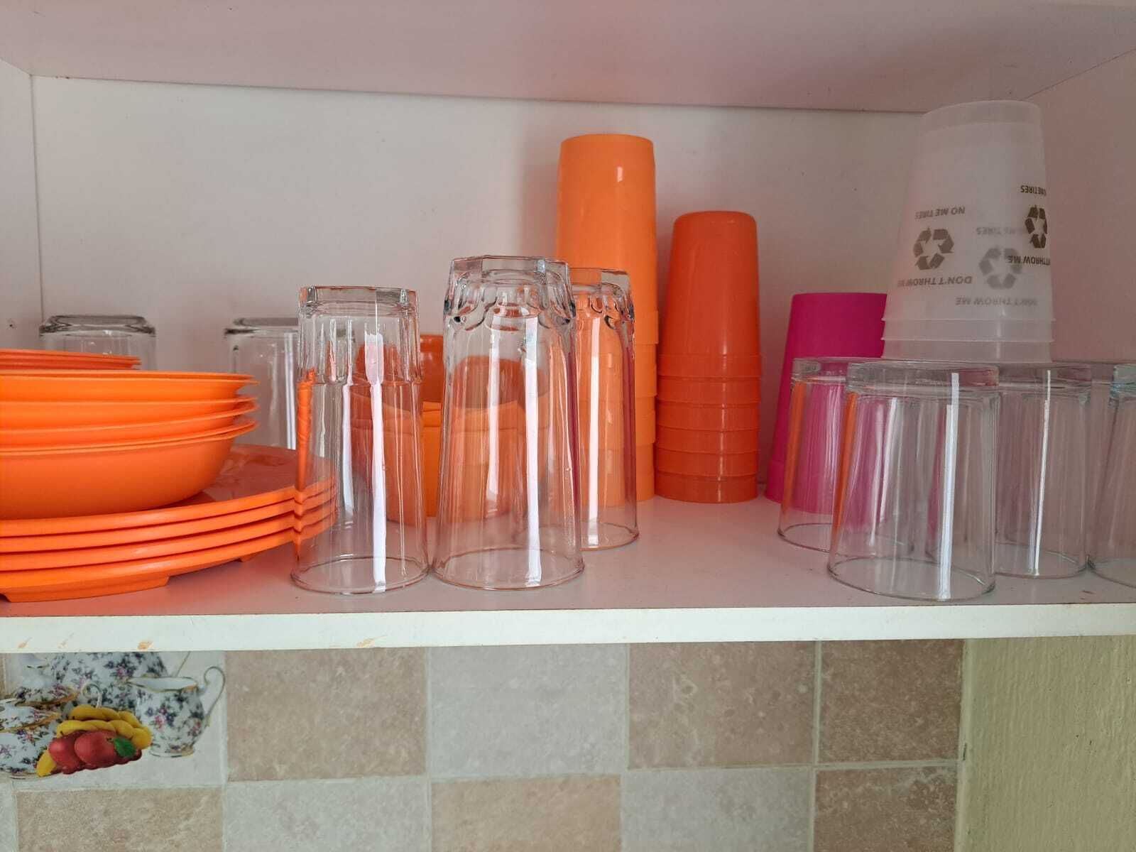 Keittiön hyllyllä on päällekkäin aseteltuja oransseja lautasia, läpinäkyviä lasipurkkeja sekä oransseja ja vaaleanpunaisia säilytysastioita.