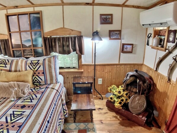 Una habitación acogedora con cama, mesa, lámpara y decoración rústica, incluyendo paredes de madera y una estufa antigua.