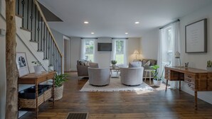 Un salón espacioso con una escalera, suelo de madera y una zona de estar acogedora con dos sillones y un sofá.