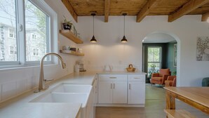 Una cocina moderna con armarios blancos, un lavamanos de acero inoxidable, luces colgantes y vistas al área de estar.