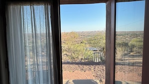 A room with a large window, curtains, and a view of a landscape with trees and a distant building. - Unique top of the world straw bale cottage has ASTOUNDING views. (Catalina)
