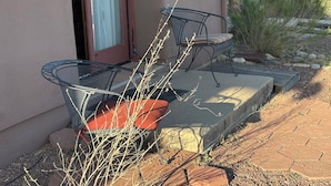 A patio with two metal chairs and a red cushion, a concrete bench, and a view of a desert landscape. - Unique top of the world straw bale cottage has ASTOUNDING views. (Catalina)