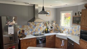 A modern kitchen with a central island, wooden cabinets, a stainless steel refrigerator, and a window providing natural light. - Family home between the sea and the Cevennes (Calvisson)