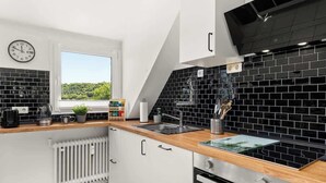 A modern kitchen with a black tiled backsplash, white cabinetry, a built-in oven, and a window offering a view of greenery. - MOLA Apartments-Style & Flair (Wetter (Ruhr))