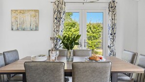 Uma sala de jantar com uma mesa posta para quatro pessoas, um vaso com plantas verdes e uma garrafa de vinho.