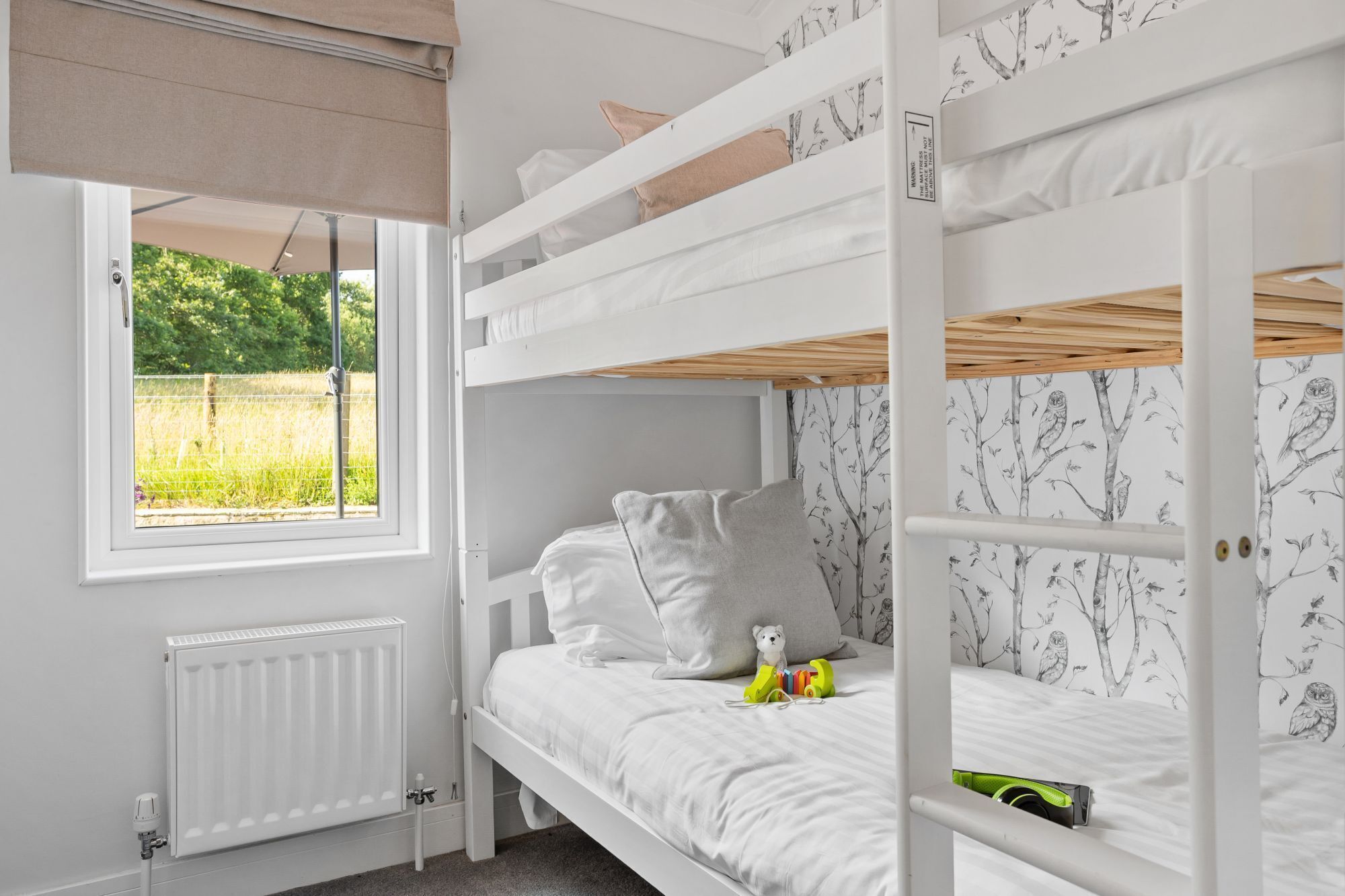 A bunk bed room with a window, a radiator, and a wall with a tree and owl pattern.