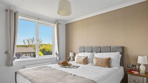 Quarto com cama grande, mesa de cabeceira, luminária e janela com cortinas.