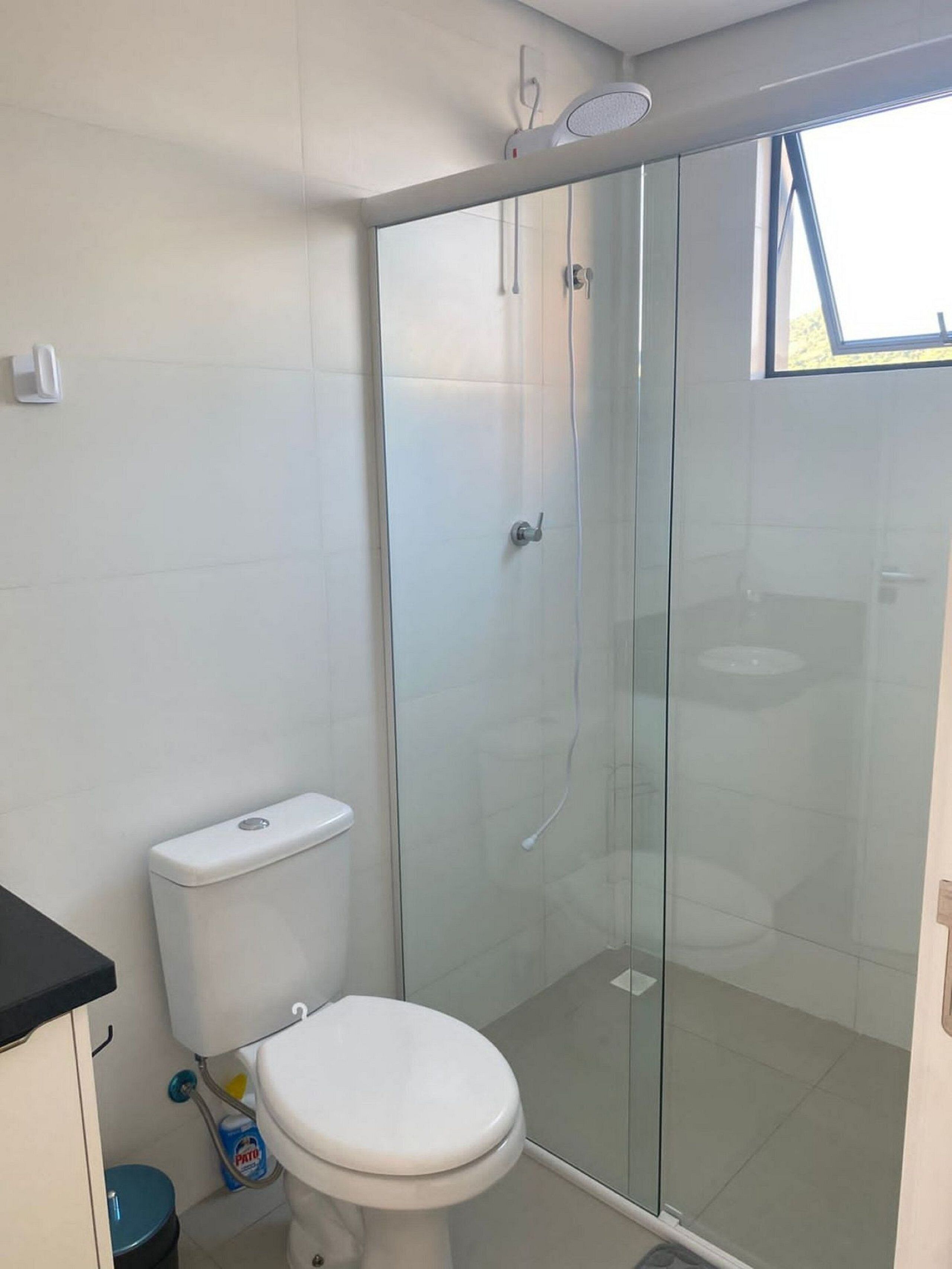 Une salle de bain moderne équipée de toilettes, d’une douche à parois de verre et d’une fenêtre laissant entrer la lumière naturelle.