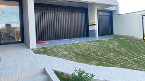 Un edificio moderno con un acceso cubierto, un patio con césped y una escalera visible que conduce a la entrada.