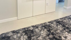 Una sala moderna con un televisor de pantalla plana montado en un mueble blanco, un equipo de aire acondicionado encima y una alfombra gris y mullida en el suelo.