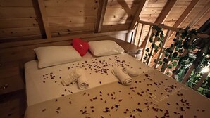 Ein Schlafzimmer einer Holzhütte mit einem Bett, Kissen, einem herzförmigen Luftballon und verstreuten Rosenblättern.