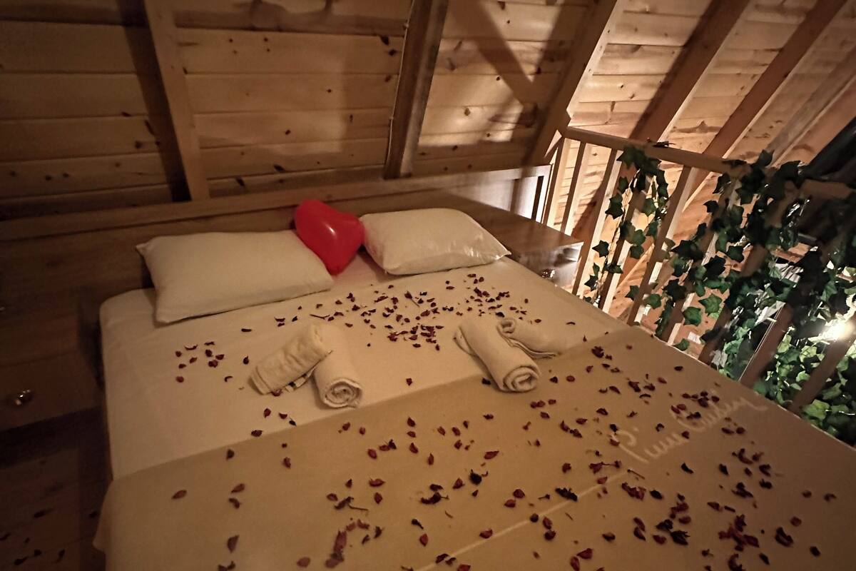 A wooden cabin bedroom with a bed, pillows, heart-shaped balloon, and scattered rose petals.