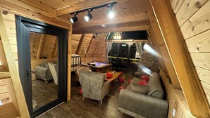 Une pièce mansardée chaleureuse avec des murs en bois, un placard avec une porte miroir, un canapé, un fauteuil et une petite table.