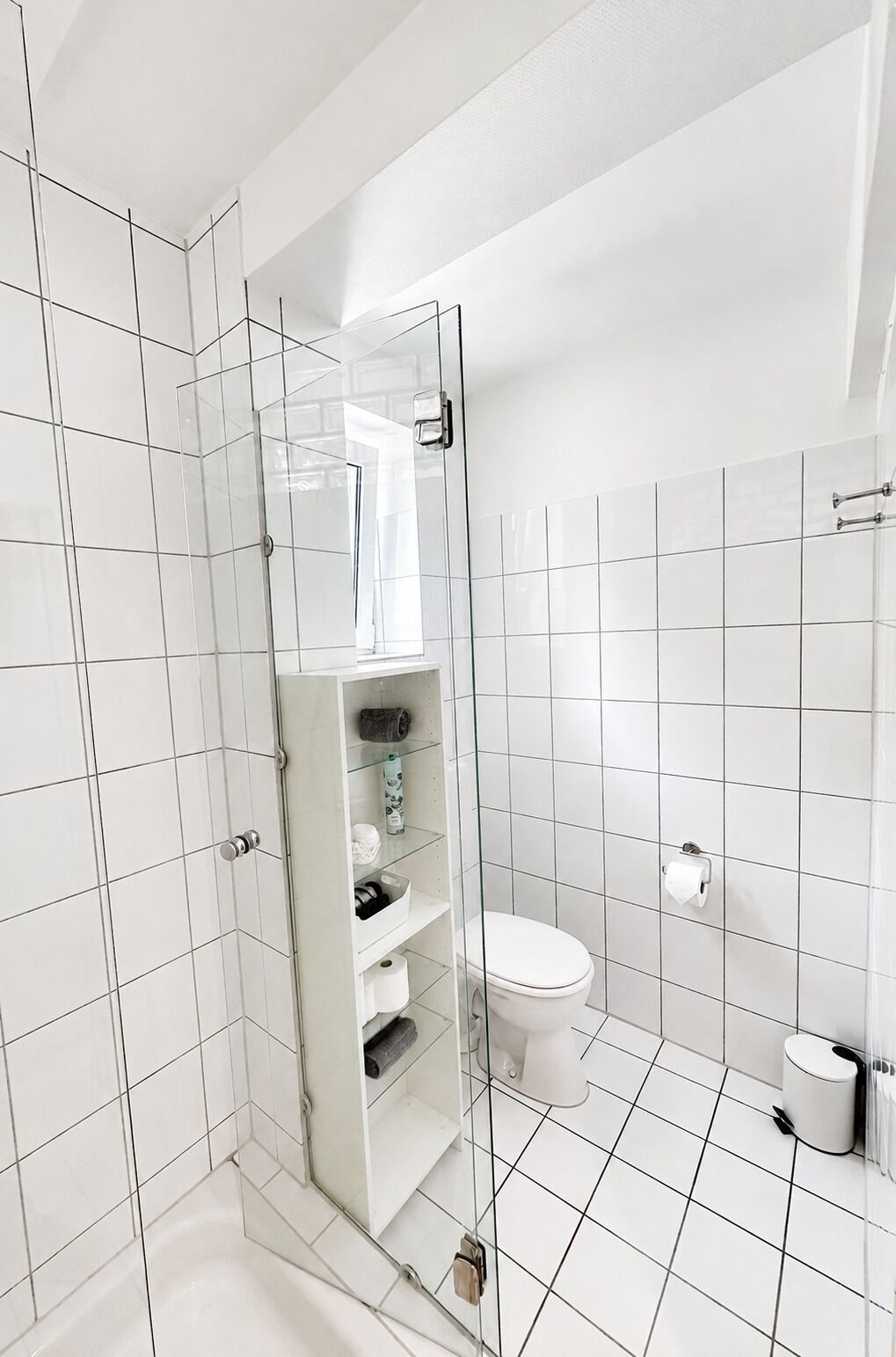 A modern bathroom with a glass-enclosed shower, white tiled walls, and a toilet.