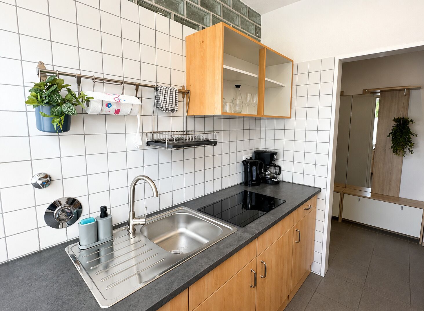 Eine moderne Küche mit Spüle aus Edelstahl, Holzschränken, einer schwarzen Arbeitsplatte und einer Kaffeemaschine.