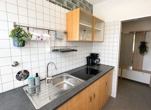 A modern kitchen with a stainless steel sink, wooden cabinets, a black countertop, and a coffee maker.