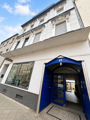 A building with a blue entrance, a visible shop window with bicycles, and a sign indicating a school.