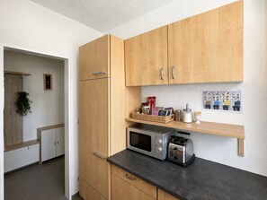 A modern kitchen with wooden cabinets, a microwave, a toaster, and a small shelf with kitchen items.