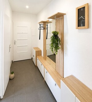 Een hal met een houten bankje, een spiegel met een plant en een wandklok.