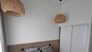 Un dormitorio con una cama, dos lámparas colgantes de mimbre, un armario y un cabecero de madera.