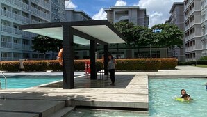 A swimming pool area with a covered seating area and steps leading into the pool. - Home-Away FromHome@ Trees  Residences QC (Quezon City)
