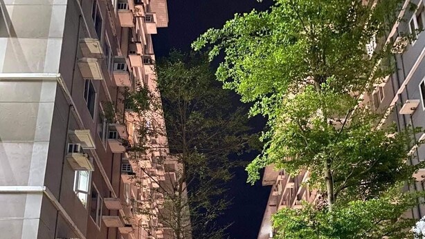 A nighttime view of a residential building with multiple floors, balconies, and a well-lit central area with plants and a bench. - Home-Away FromHome@ Trees  Residences QC (Quezon City)