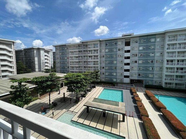 A modern apartment building with multiple balconies, a rooftop pool, and a landscaped courtyard. - Home-Away FromHome@ Trees  Residences QC (Quezon City)