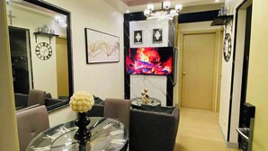 A modern living room with a glass-top dining table, a chandelier, a fireplace, and a large mirror. - Home-Away FromHome@ Trees  Residences QC (Quezon City)