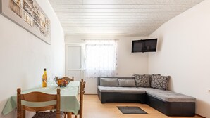 A cozy living room with a dining area, a sofa, and a flat-screen TV mounted on the wall.