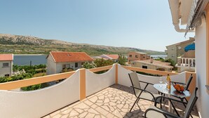 A balcony with a table and chairs, overlooking a body of water and hills.