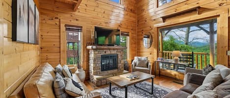 L’intérieur d’un chalet en bois comprend une cheminée, un coin salon et une grande fenêtre donnant sur l’extérieur.