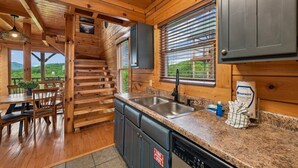 A wooden cabin interior with a kitchen area, dining space, and a staircase leading to an upper level. - Sky High Smoky Mountain Retreat w/ Views (Sevierville)