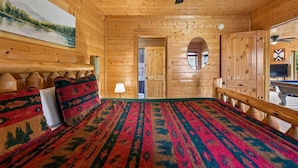 A wooden cabin room with a bed, a ceiling fan, a painting, and a door leading to another room. - Sky High Smoky Mountain Retreat w/ Views (Sevierville)