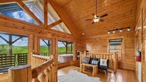 A wooden cabin interior with a wooden ceiling, a ceiling fan, a sofa with cushions, a white rug, and a view of the outdoors. - Sky High Smoky Mountain Retreat w/ Views (Sevierville)