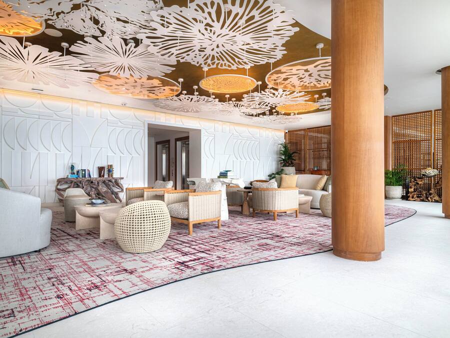 Un vestíbulo amplio con mobiliario moderno, alfombra estampada y paneles decorativos en el techo.