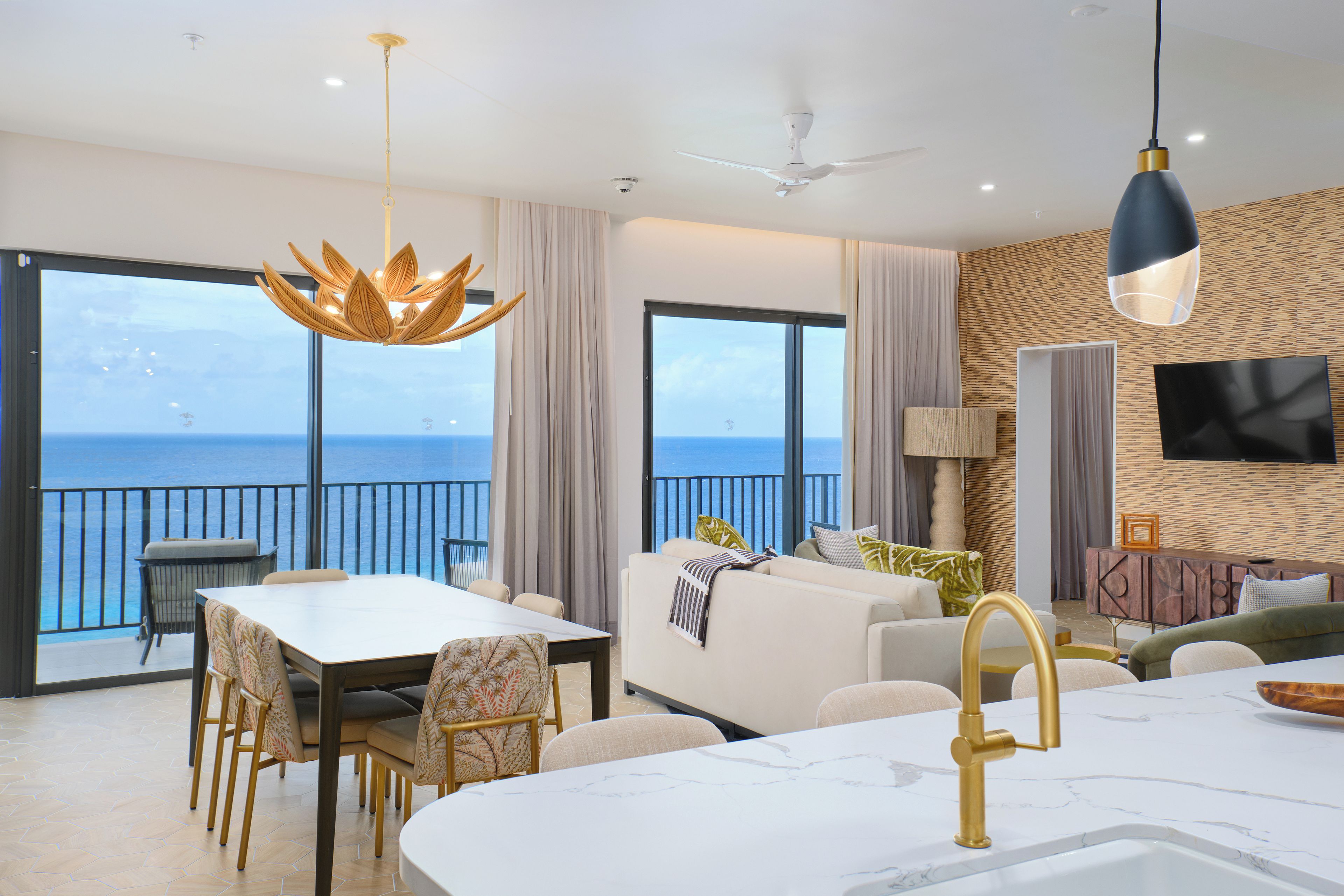 Een moderne woonkamer met een balkon met uitzicht op zee, een eethoek met tafel en stoelen, en een keuken met een marmeren aanrecht.