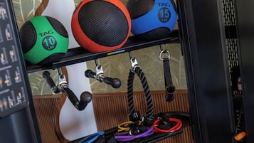 Un estante con equipo de ejercicio, incluyendo una pelota medicinal TAG de 10 libras color verde y negro, una pelota medicinal roja y negra, y una pelota medicinal TAG de 15 libras color azul.
