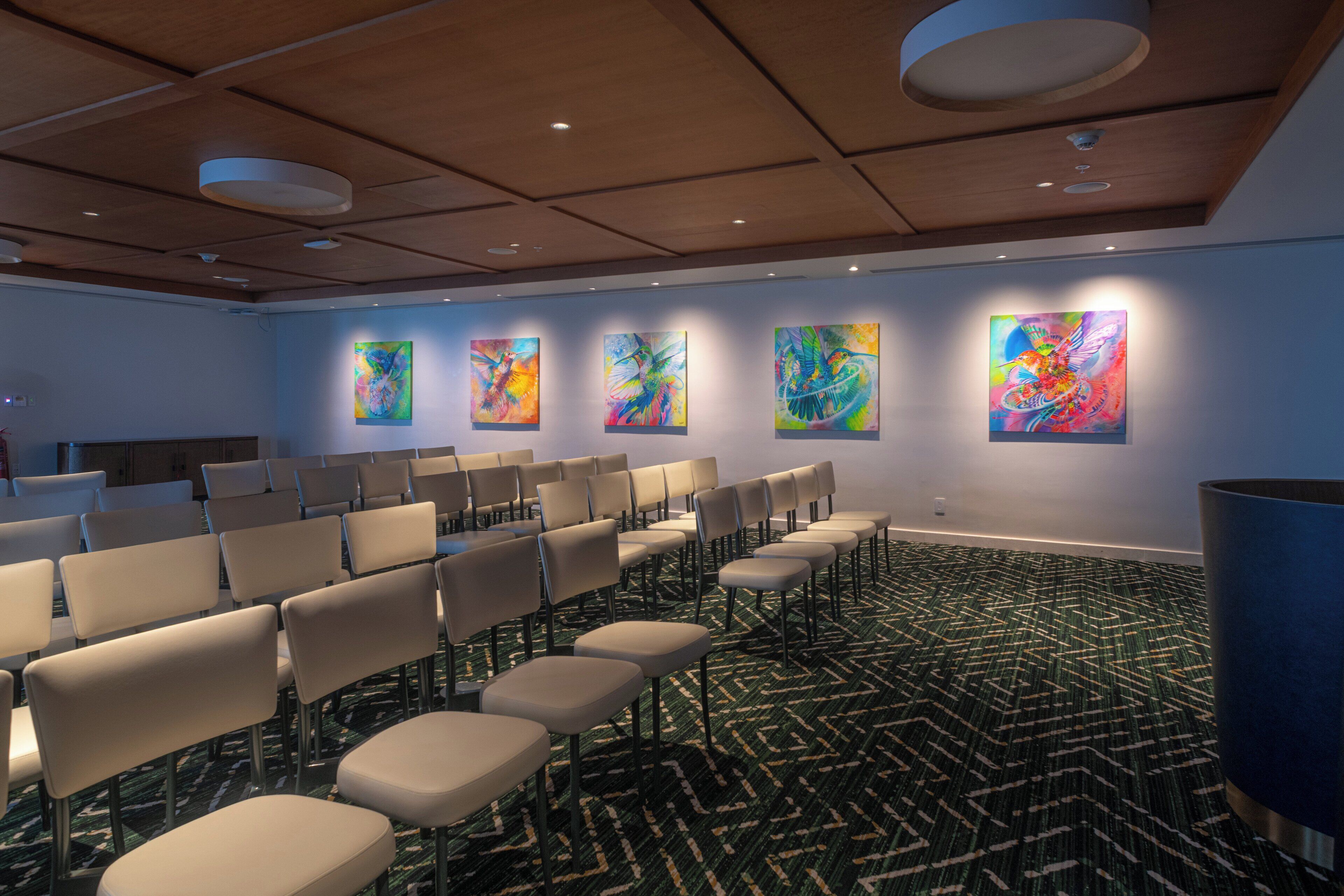 Une salle de conférence avec des rangées de chaises, une moquette à motifs et des tableaux abstraits accrochés aux murs.