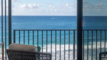 A balcony with wicker chairs and a table, overlooking a calm sea with a boat in the distance.