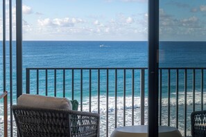 A balcony with wicker chairs and a table, overlooking a calm sea with a boat in the distance. - Hotel Indigo Bridgetown Barbados by IHG (Hastings)