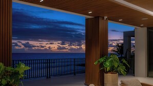 A balcony with wicker furniture, a potted plant, and a view of the ocean at dusk. - Hotel Indigo Bridgetown Barbados by IHG (Hastings)