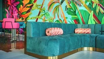 A teal sofa with gold trim, two patterned cushions, and a vibrant tropical mural in the background.