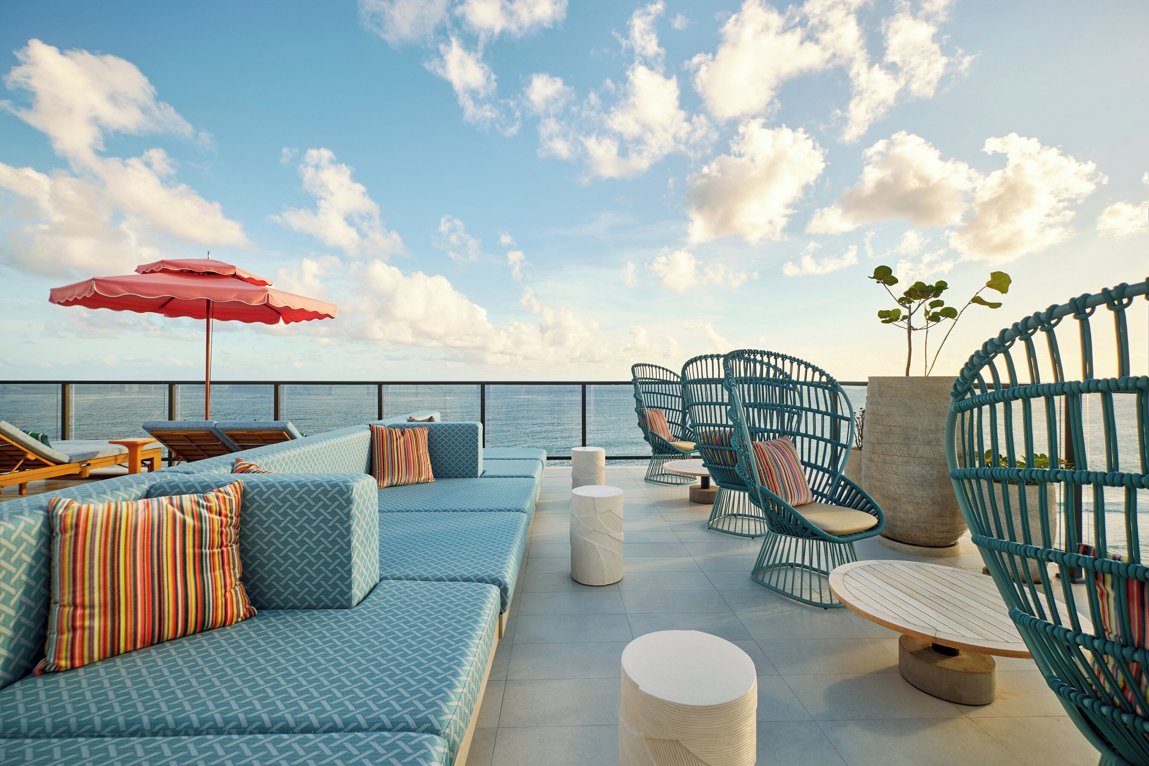 A rooftop lounge with seating, a red umbrella, and a view of the sea.