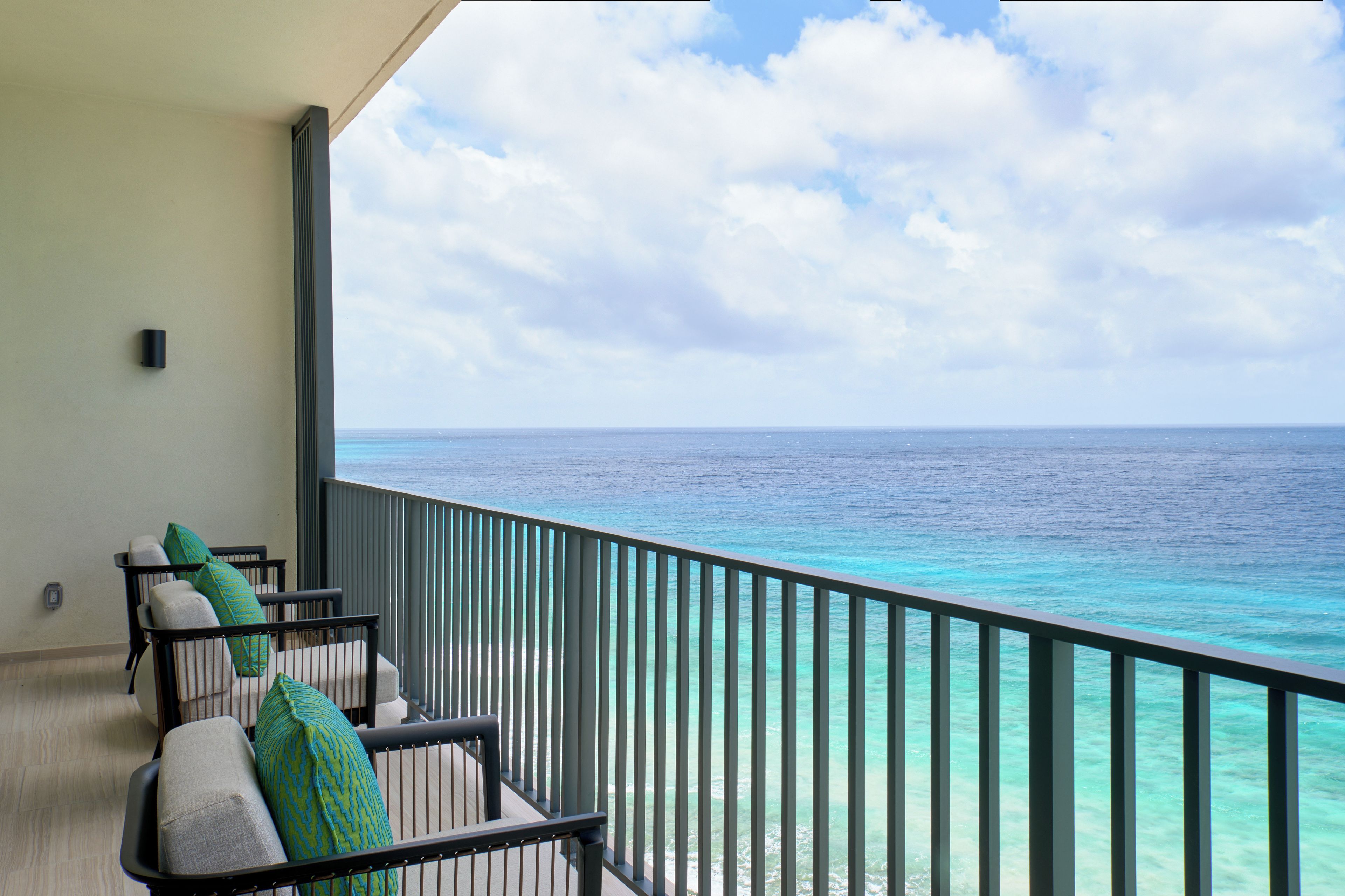 Een balkon met uitzicht op de oceaan, met een hekwerk en zitplaatsen met kussens.