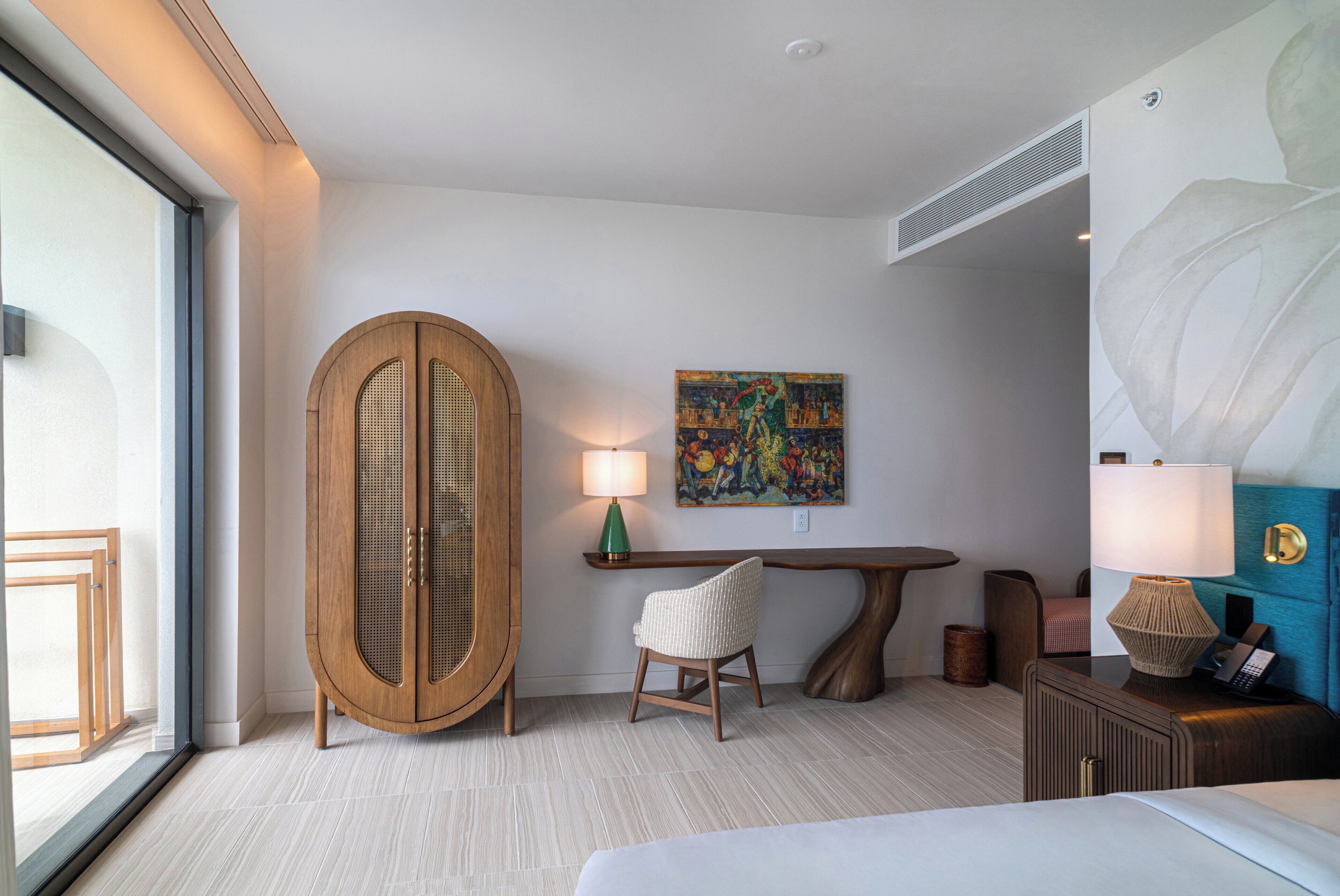 Habitación de hotel con un armario de madera grande, una silla pequeña, una mesa, una lámpara y un cuadro en la pared.